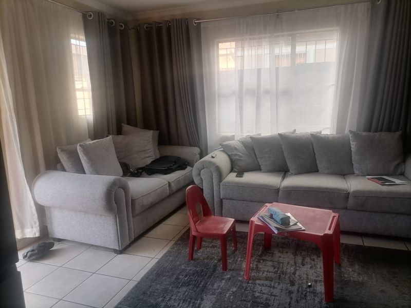 A comfortable living room featuring tiled flooring, large windows with curtain rails, and security bars for added peace of mind.