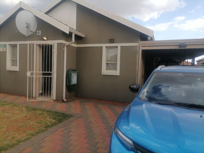 Front elevation of the house featuring a paved driveway, attached carport, and secure entrance with a metal security gate.