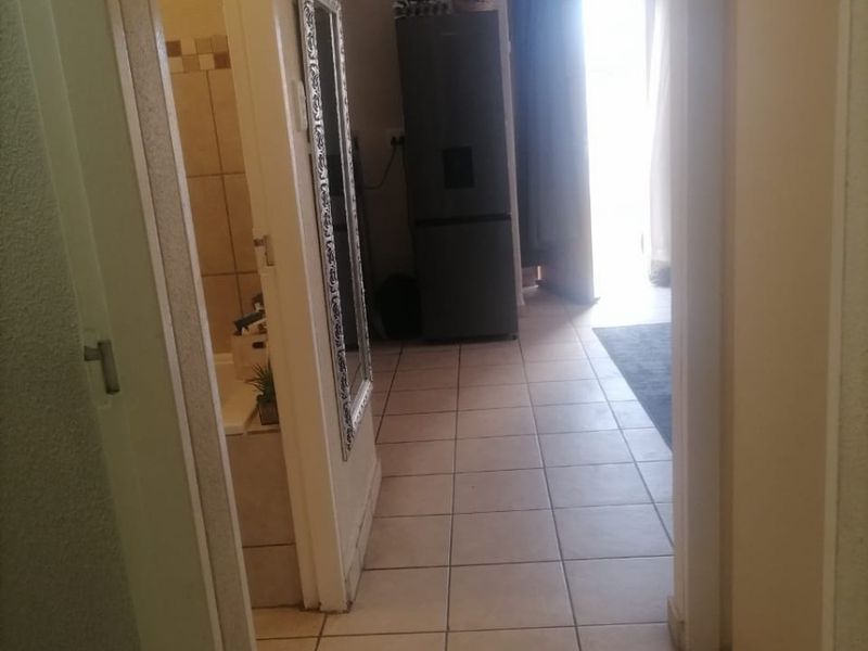 A tiled hallway providing access to a bathroom and an adjacent living area with natural light.