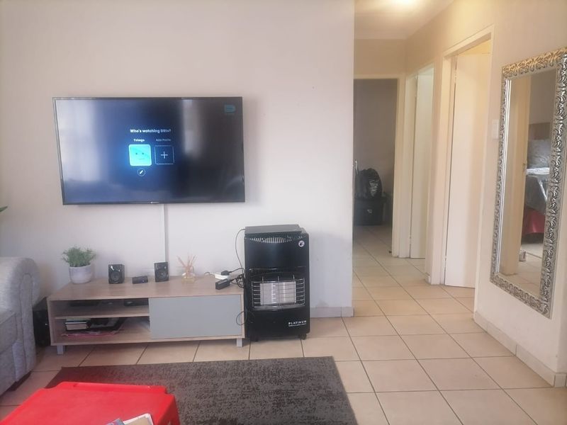 A living room featuring tiled flooring, a wall-mounted television, and access to a hallway leading to other areas of the home.