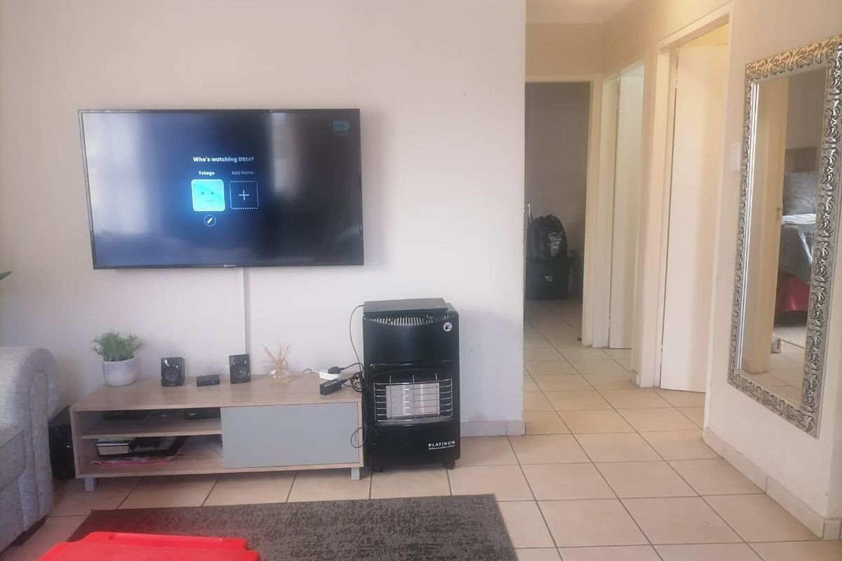 A living room featuring tiled flooring, a wall-mounted television, and access to a hallway leading to other areas of the home.