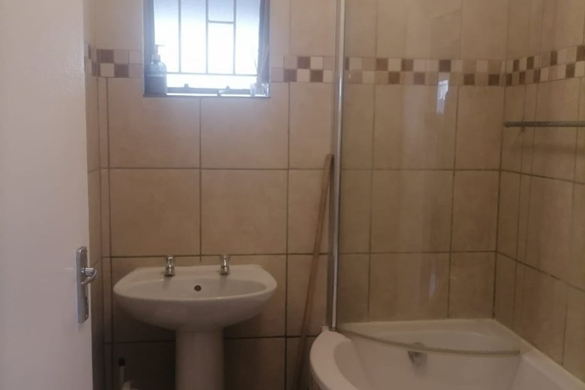 A compact bathroom featuring a pedestal basin and a shower-over-bath combination with a glass screen, finished with neutral wall and floor tiling.