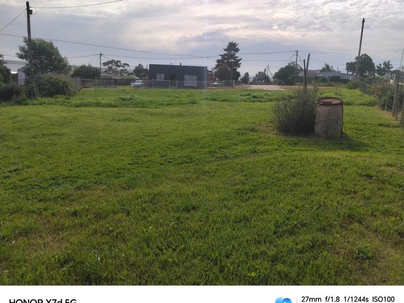 A vacant residential plot featuring open grass, perimeter fencing, and utility infrastructure, offering a clear space for potential development.