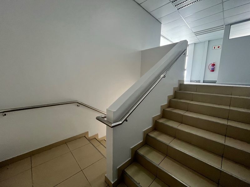 A clean, well-maintained industrial staircase featuring tiled steps, stainless steel handrails, and a suspended ceiling with integrated fire safety equipment.