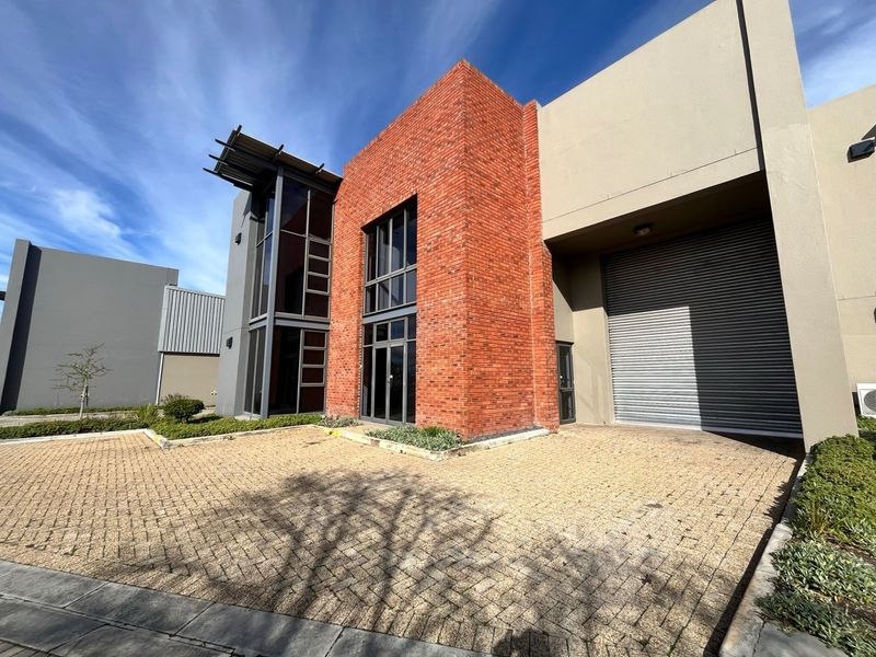 Modern industrial unit featuring a striking red brick facade, large glass windows, and a secure roller shutter door with paved exterior access.
