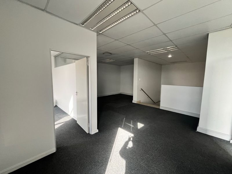 An open-plan office space featuring a suspended ceiling with recessed lighting, carpeted flooring, and a staircase leading to another level.