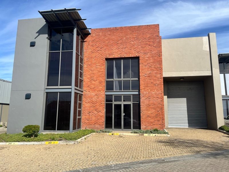 Modern industrial unit featuring a striking red brick facade, large glass windows, and a secure roller shutter door with paved driveway access.