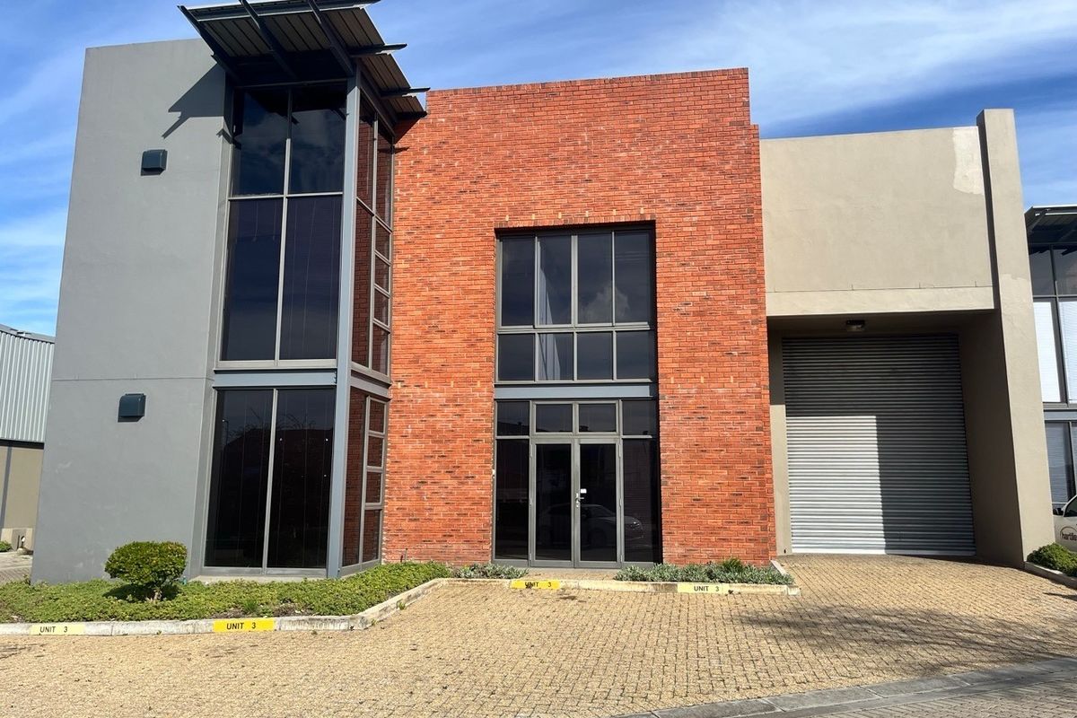 Modern industrial unit featuring a striking red brick facade, large glass windows, and a secure roller shutter door with paved driveway access.