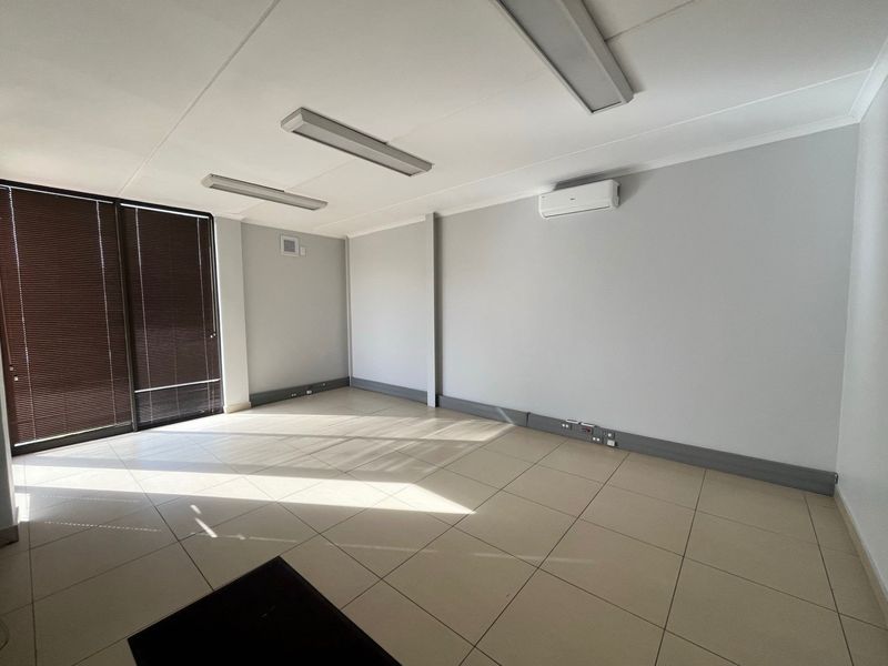 A clean, empty office space featuring tiled flooring, wall-mounted air conditioning, and integrated electrical trunking, suitable for a professional workspace.