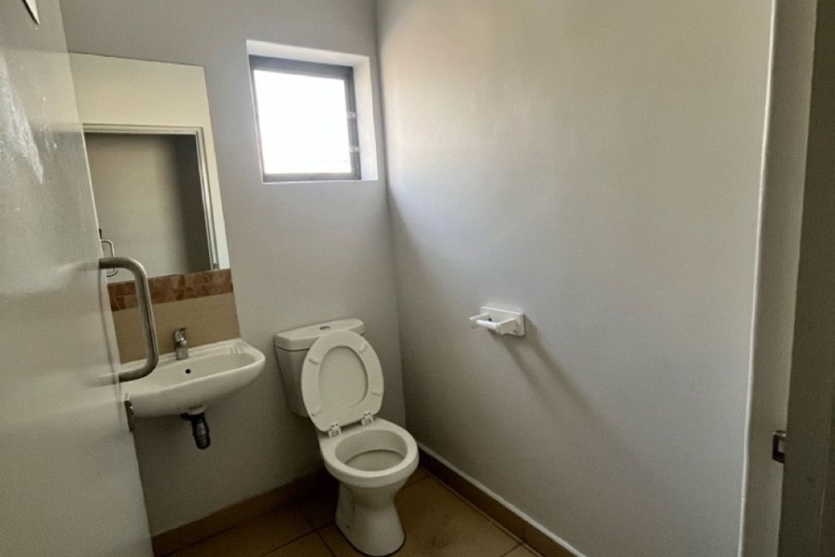 A functional, compact industrial-style restroom featuring a wall-mounted basin, toilet, and tiled flooring.