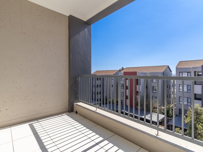 A clean, modern balcony featuring tiled flooring and a secure metal balustrade, offering an open view of the surrounding apartment complex.