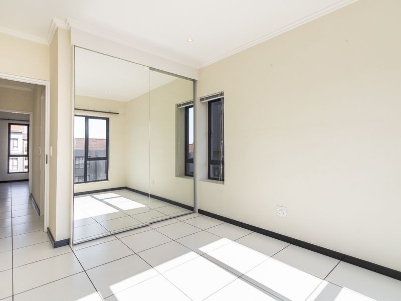 A bright, empty bedroom featuring large built-in mirrored wardrobes, neutral tiled flooring, and modern aluminium window frames.
