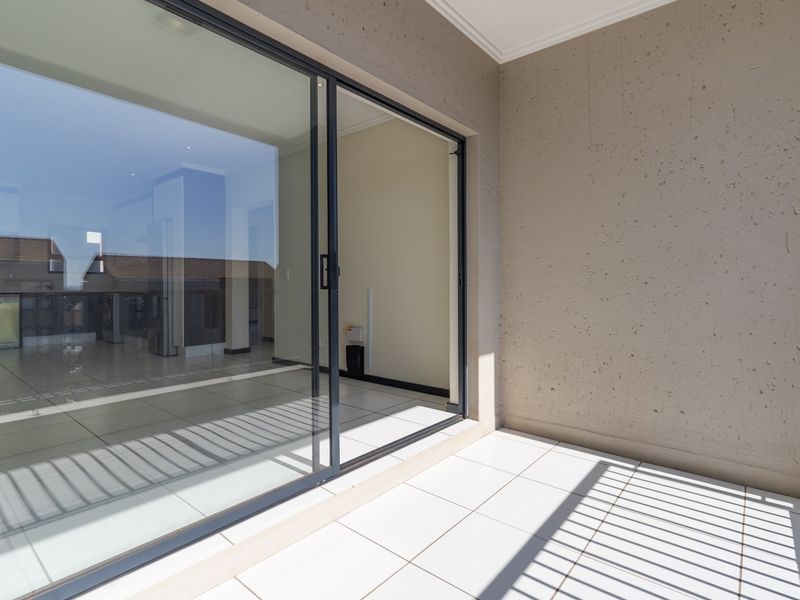 A clean, modern balcony featuring white tiled flooring, textured walls, and a large sliding glass door providing access to the interior living space.
