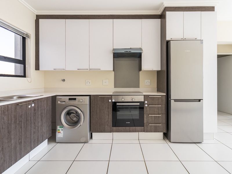 Modern kitchen featuring two-tone cabinetry, stone countertops, integrated stainless steel appliances, and clean white tiled flooring in a bright, open layout.