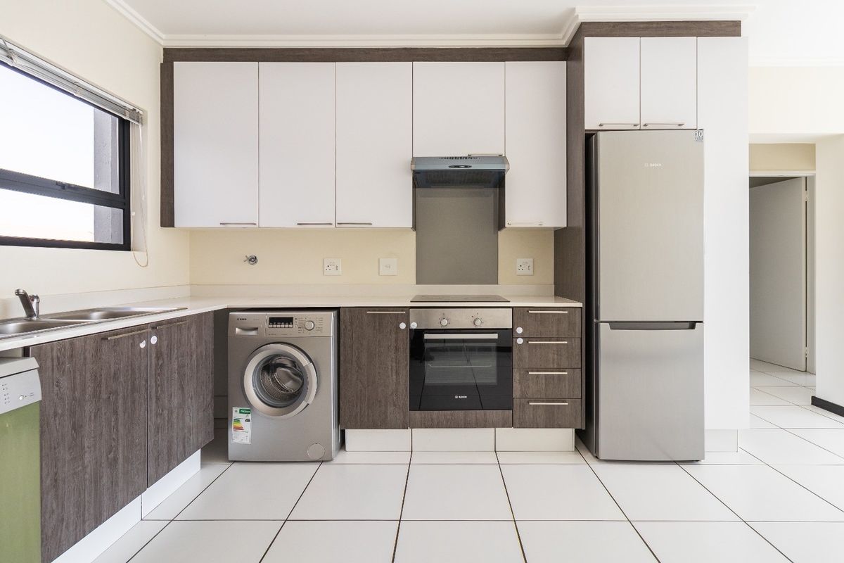 Modern kitchen featuring two-tone cabinetry, stone countertops, integrated stainless steel appliances, and clean white tiled flooring in a bright, open layout.