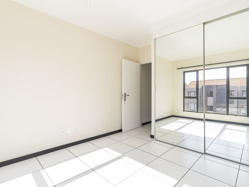 A bright, empty bedroom featuring large built-in mirrored wardrobes, modern tiled flooring, and large windows allowing for ample natural light.