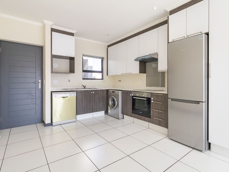 Modern kitchen featuring two-tone cabinetry, stone countertops, integrated oven, extractor fan, and tiled flooring with space for under-counter appliances.