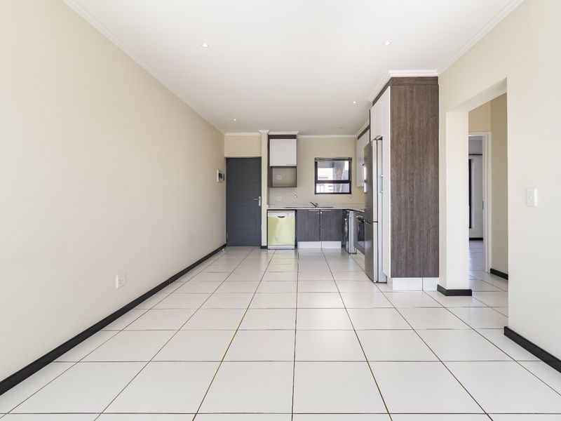 An open-plan living and kitchen area featuring neutral tiled flooring, modern cabinetry, and recessed lighting, offering a clean and versatile space.