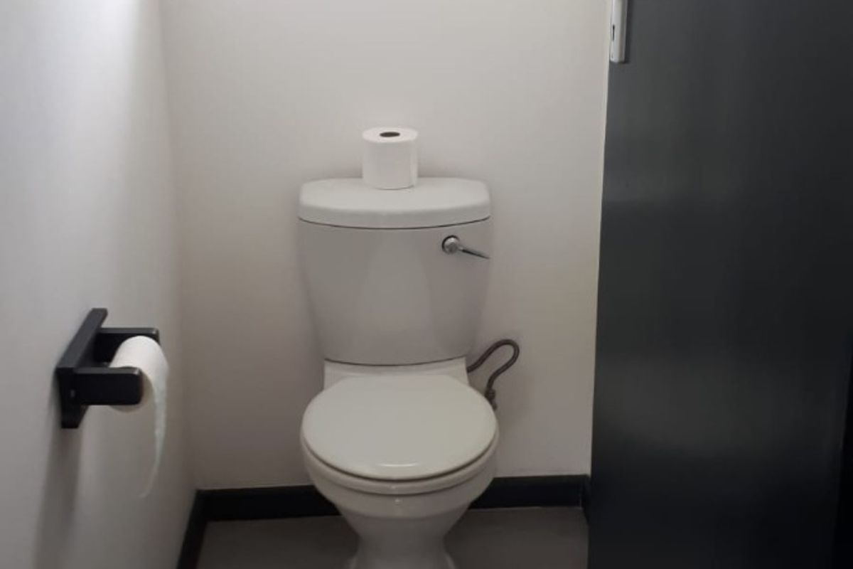 A clean and functional guest toilet featuring modern grey floor tiles, a white toilet suite, and a dark door.