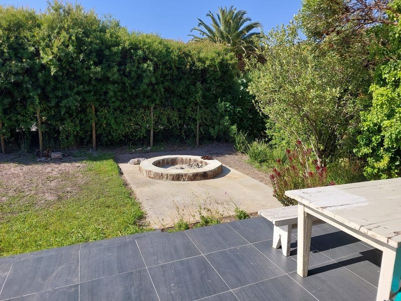 A private garden area featuring a stone fire pit, concrete patio base, and dark tiled flooring, surrounded by established hedges.