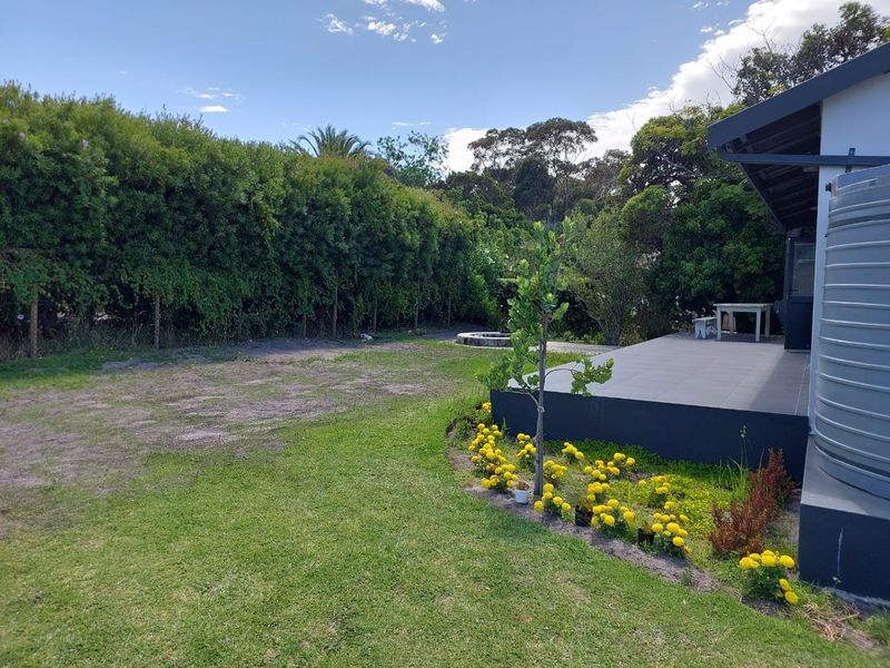 A spacious rear garden featuring a tiled patio area, established hedge boundaries, and a large water storage tank.