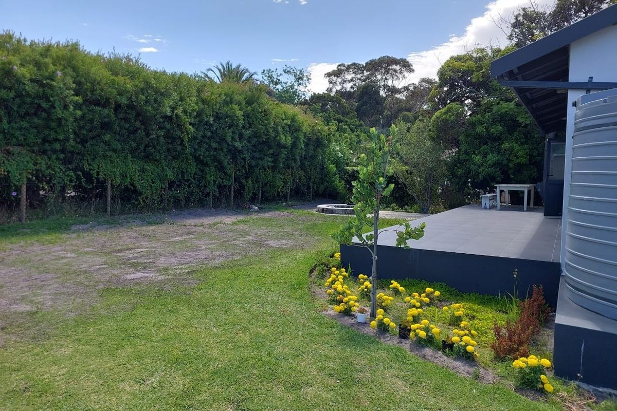 A spacious rear garden featuring a tiled patio area, established hedge boundaries, and a large water storage tank.