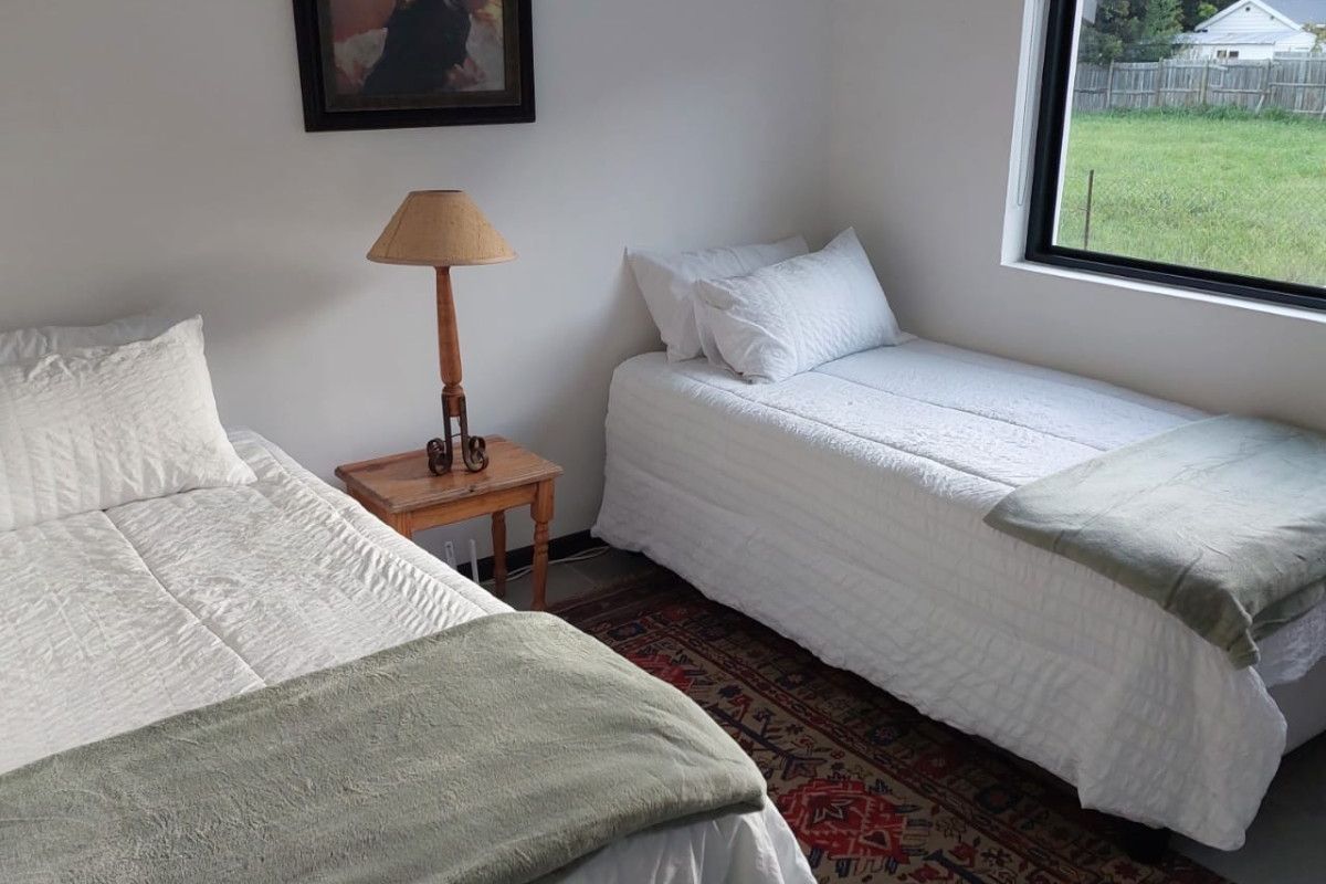 A bright bedroom featuring neutral walls, a large window with a roller blind, and ample space for twin beds.
