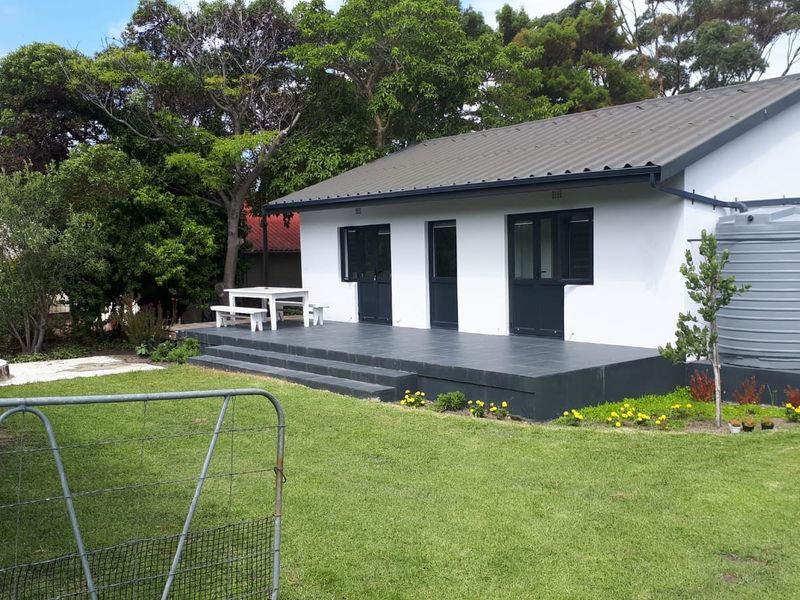 A well-maintained rear exterior view of the house featuring a tiled patio, dark-framed doors, and a large water storage tank set in a garden.