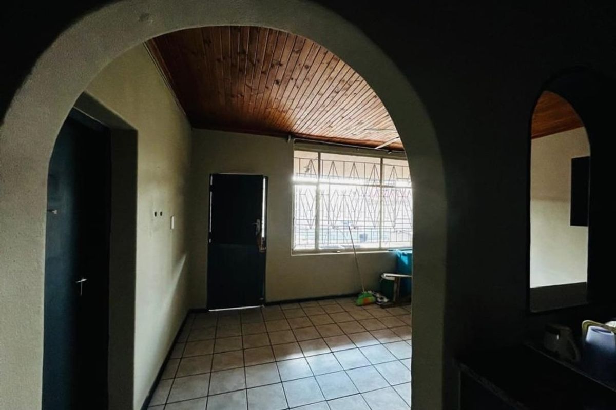 An empty living area featuring tiled flooring, a timber-paneled ceiling, and an arched entryway, providing a blank canvas for renovation.