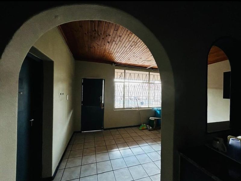 An empty living area featuring tiled flooring, a timber-paneled ceiling, and an arched entryway, providing a blank canvas for renovation.