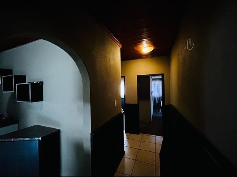 A dimly lit hallway featuring tiled flooring, timber ceiling panels, and an arched entryway leading into adjacent living spaces.