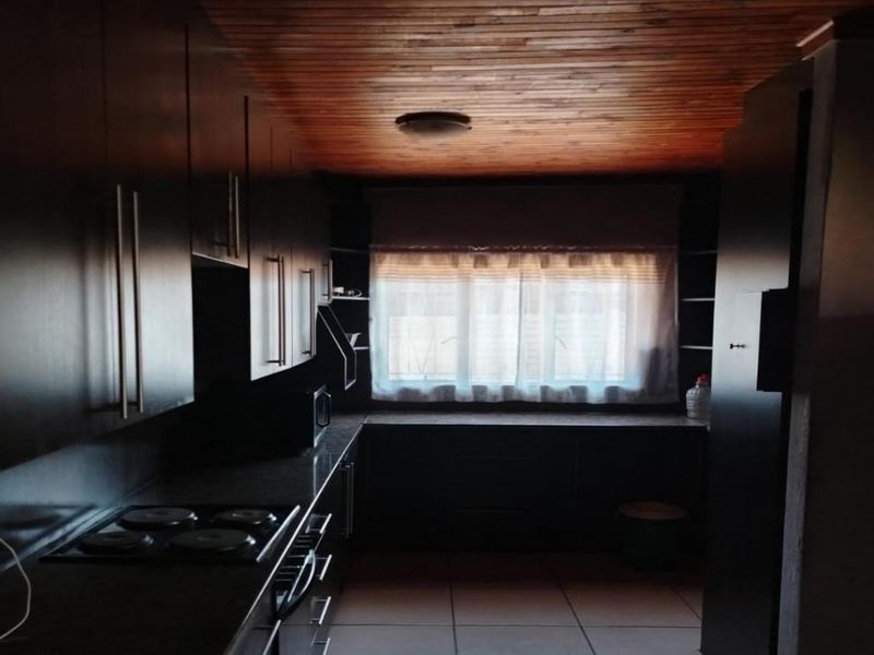 A functional kitchen featuring dark built-in cabinetry, an electric hob, tiled flooring, and a distinctive timber-paneled ceiling.