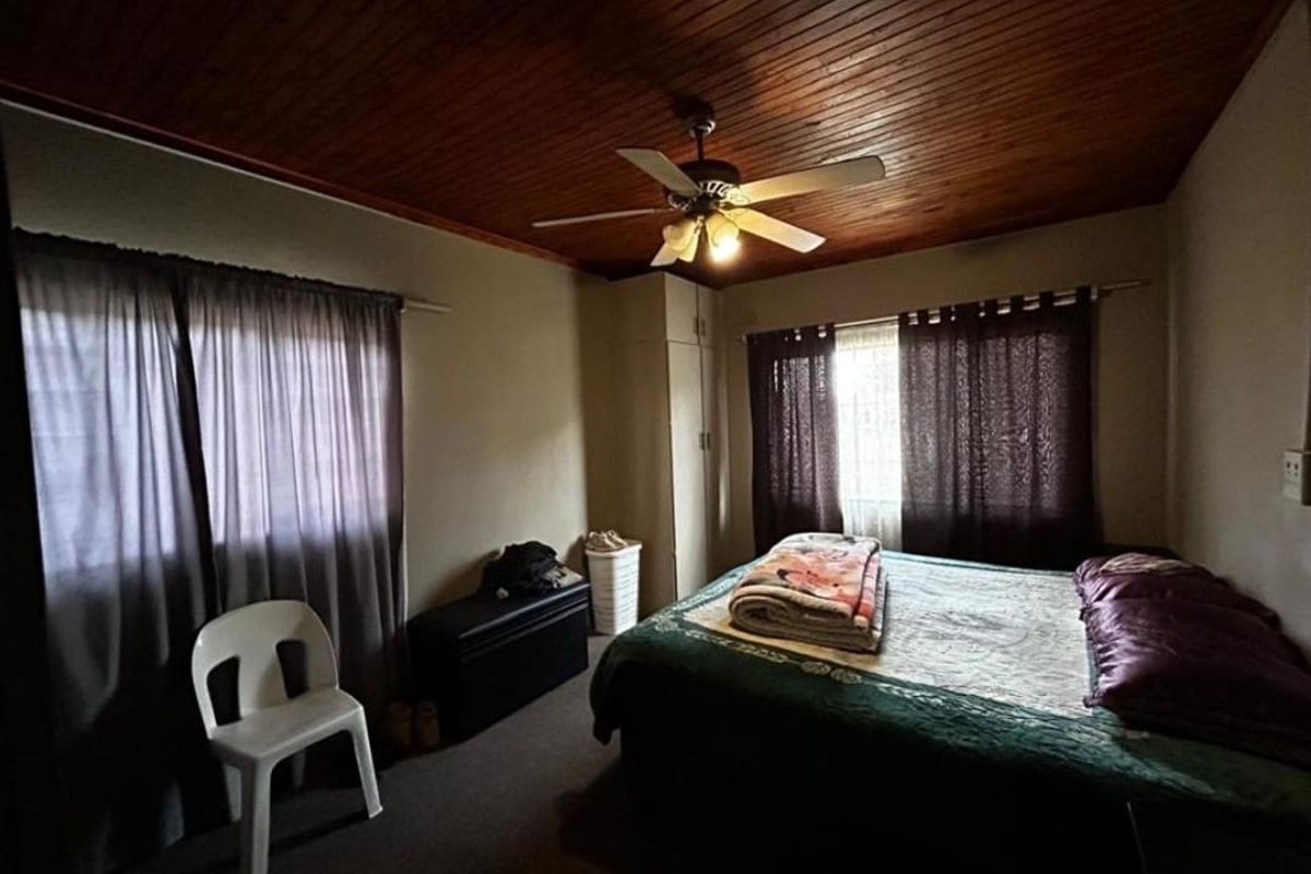 A bedroom featuring a timber-paneled ceiling, a central ceiling fan, and built-in wardrobe storage.