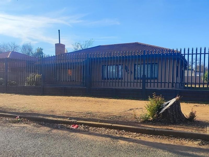 Front view of a single-story house featuring a tiled roof, brick chimney, and secure metal perimeter fencing with security bars on the windows.
