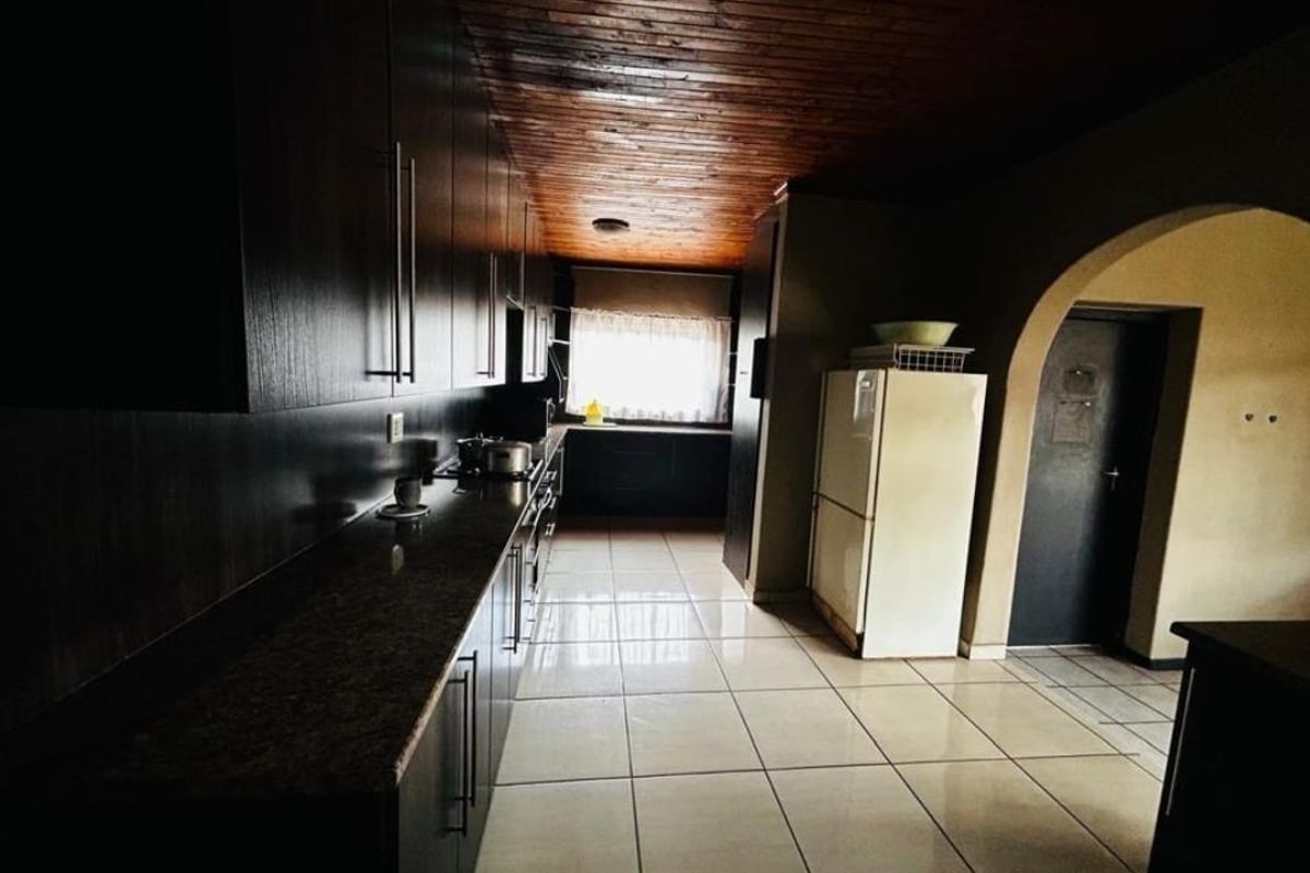 A kitchen featuring dark wood cabinetry, granite countertops, tiled flooring, and a distinctive timber plank ceiling with an arched entryway.