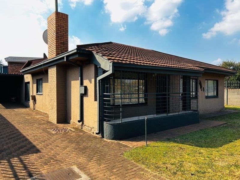 Front exterior view of a single-story house featuring a brick chimney, tiled roof, paved driveway, and security bars on windows.