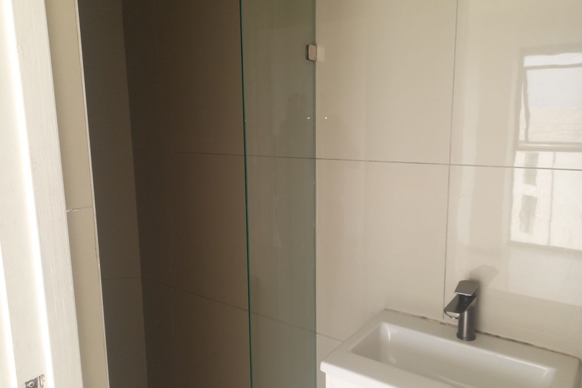 A compact bathroom featuring a modern wall-mounted basin with a mixer tap and a glass shower screen with tiled walls.