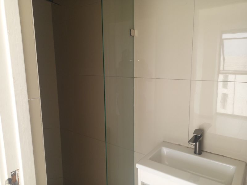 A compact bathroom featuring a modern wall-mounted basin with a mixer tap and a glass shower screen with tiled walls.