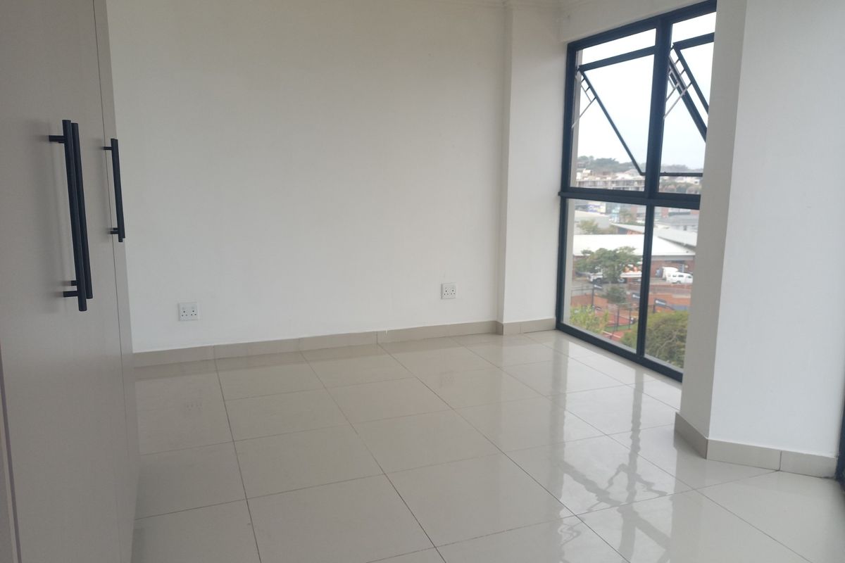 A bright, empty bedroom featuring neutral tiled flooring, a built-in wardrobe, and large aluminium-framed windows offering an elevated view.