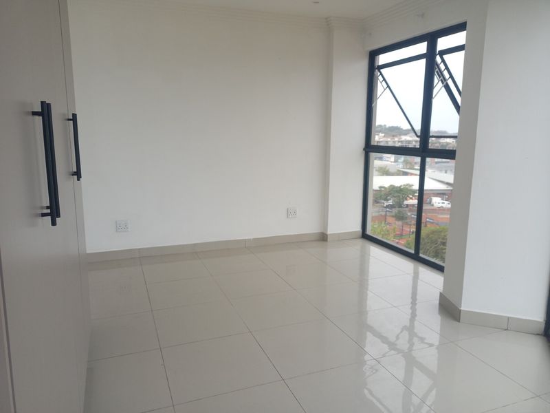 A bright, empty bedroom featuring neutral tiled flooring, a built-in wardrobe, and large aluminium-framed windows offering an elevated view.