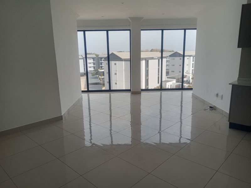 Spacious, light-filled open-plan living area featuring large floor-to-ceiling windows, polished tile flooring, and a neutral modern aesthetic.