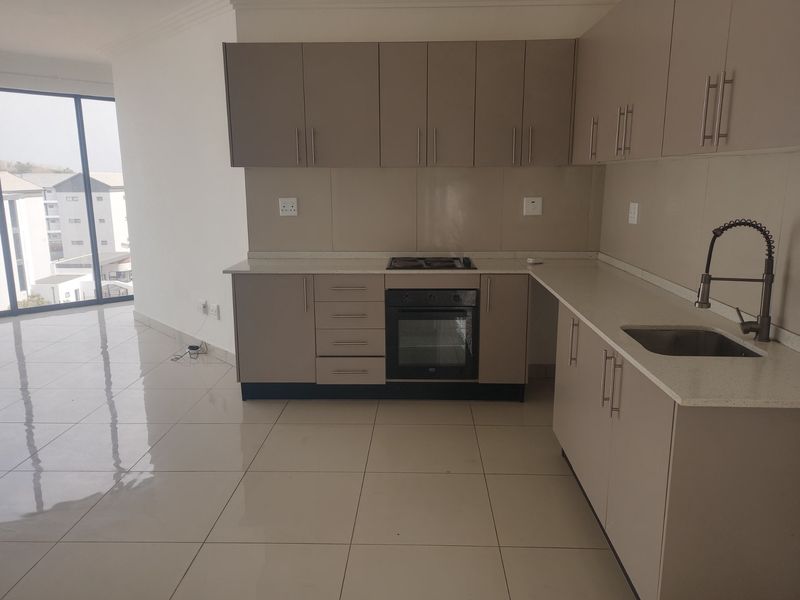 Modern kitchen featuring sleek built-in cabinetry, stone countertops, integrated oven and hob, and high-quality tiled flooring in an open-plan layout.