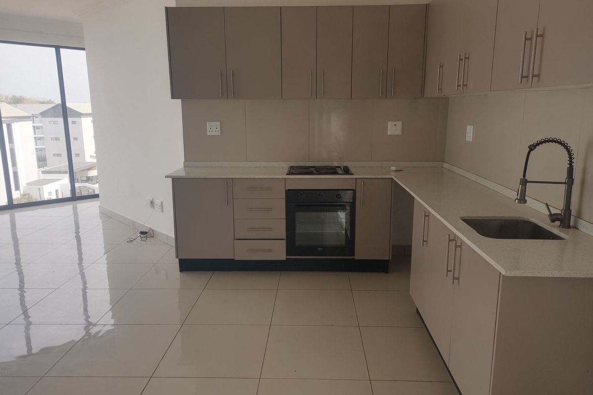 Modern kitchen featuring sleek built-in cabinetry, stone countertops, integrated oven and hob, and high-quality tiled flooring in an open-plan layout.