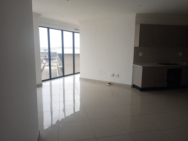 An open-plan living and kitchen area featuring modern tiled flooring, built-in cabinetry, and expansive floor-to-ceiling windows providing ample natural light.