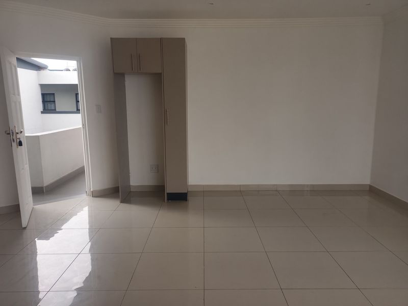 An empty, well-maintained living area featuring neutral tiled flooring, coved ceilings, and built-in storage cabinetry, with direct access to an outdoor balcony.