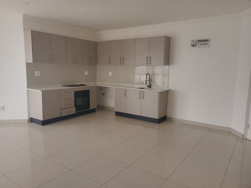 A modern, empty kitchen featuring neutral-toned cabinetry, built-in oven and hob, tiled flooring, and ample counter space in an open-plan layout.