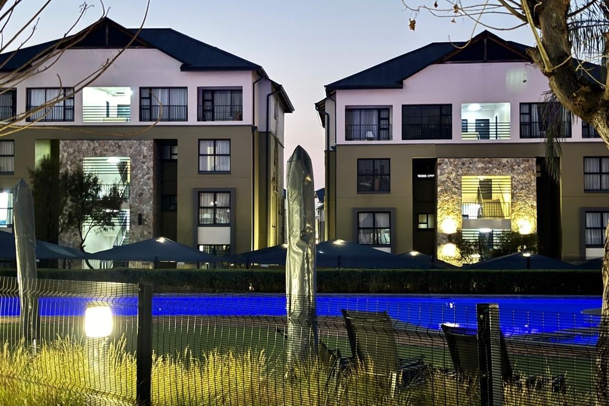 View of apartment complex exterior featuring stone-clad facades, balconies, and a communal swimming pool area at dusk.