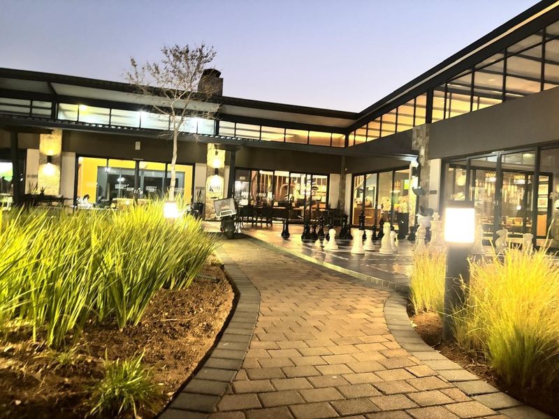 A well-maintained exterior courtyard featuring a paved walkway, landscaped garden beds, and modern architectural lighting leading to a covered patio area.
