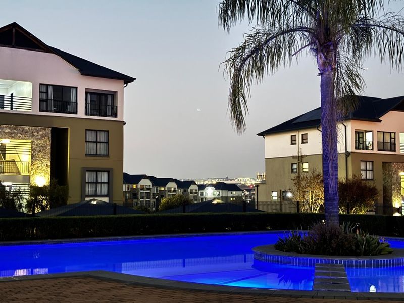 A well-maintained communal swimming pool area set within a modern apartment complex, featuring landscaped surroundings and views of the surrounding residential buildings.