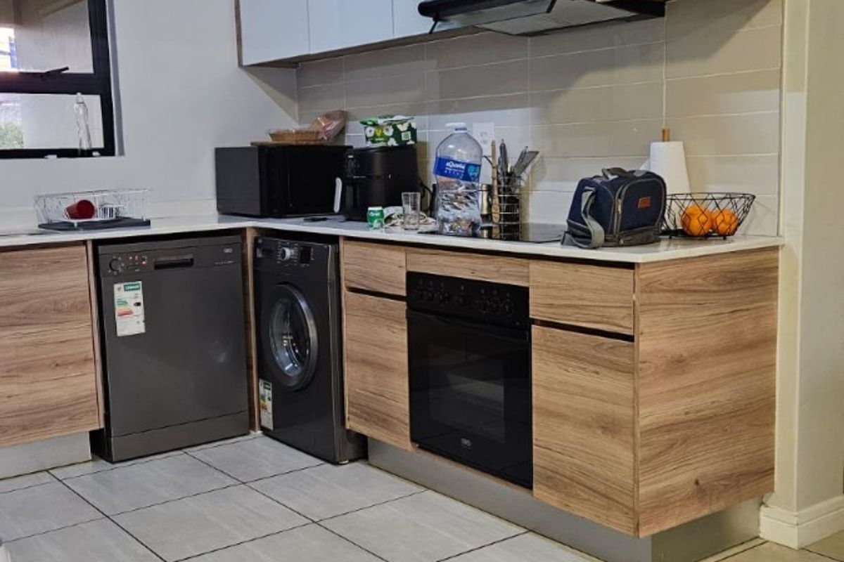 A modern kitchen featuring wood-grain and white cabinetry, stone countertops, built-in oven, extractor fan, and tiled flooring.